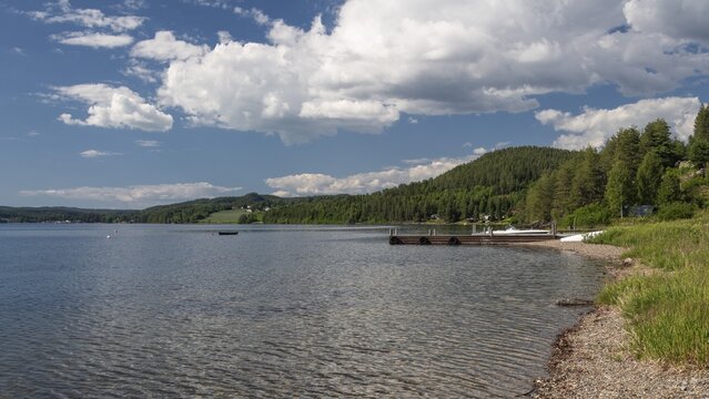 View of bathing area at Lake Mj&oslash;sa or Lake Mjosa with wooded shore under blue sky, Olavsweg or Olavsleden, near Tangen, Norway