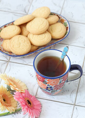 Ceramic mugs with flowers ornament with tea on the kitchen table with cookies on the background. Selective focus. 