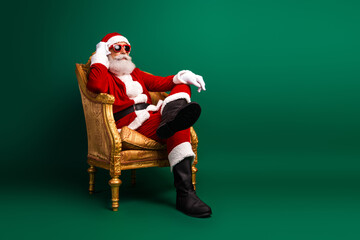 Funky Santa Claus lounging in a golden chair wearing sunglass against a green festive background, embodying seasonal charm.