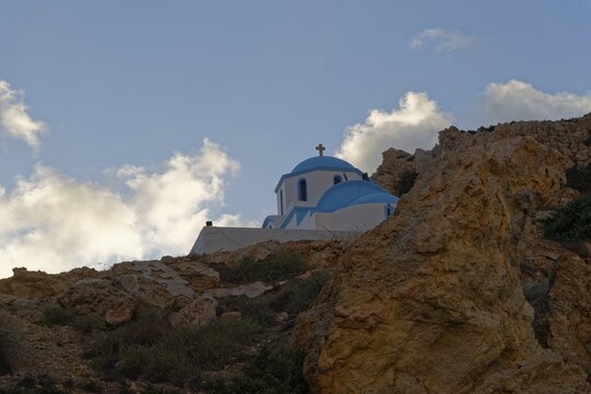 White-blue church of Agios Nikolaos with rocks in the foreground and evening sky, Finiki, Karpathos, Greece