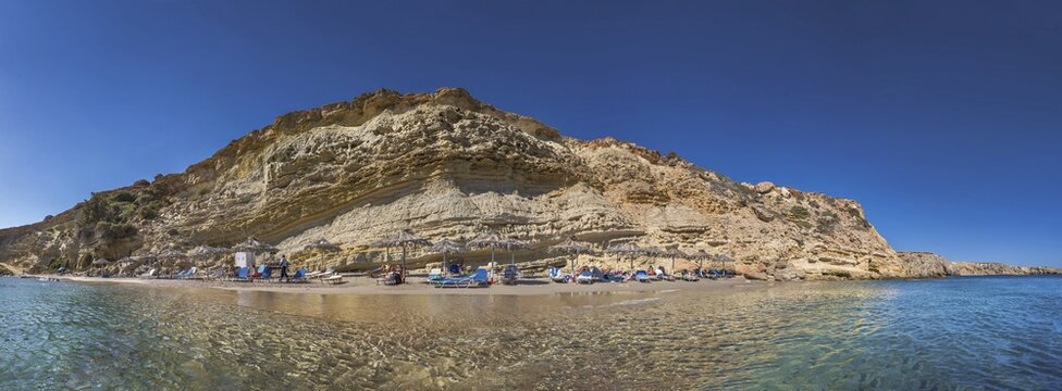 Rocky coastal landscape with Paralia Agios Theodoros sandy beach and sunshades in front of a clear sea, Arkasa, Karpathos, Greece