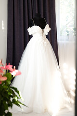 Elegant off-shoulder wedding gown displayed on a mannequin near a window.