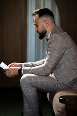 Man in suit reads a note, seated thoughtfully. A moment of contemplation.