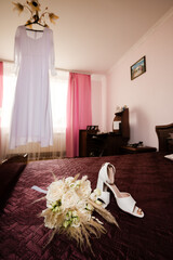 Wedding dress, bouquet, and shoes on a bed. Preparations for a special day.