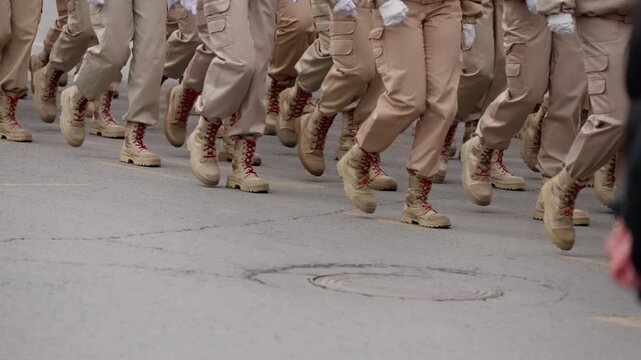 Ground-level view of uniformed personnel marching in formation on a street, combat boots and khaki trousers moving in synchronized steps highlight discipline and teamwork.