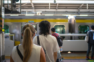 People standing in line at a Japanese train station platform, waiting for a subway train to arrive. Urban transportation, daily commuting, and modern lifestyle concept in Tokyo, Japan
