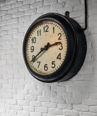 Old clock on white wall. Old analog railway clock with beige clock face and thick black bezel...