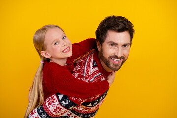 Father and daughter joyfully pose in festive sweaters on a bright yellow background, celebrating...