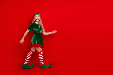 Young woman dressed as a cheerful Christmas elf posing on a vibrant red background, embodying festive holiday spirit and joy, perfect for seasonal advertising and celebration visuals