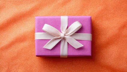 A small, rectangular pink gift box with a pale pink satin ribbon tied in a bow sits on a textured orange background