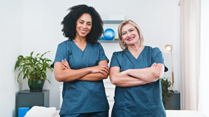 Two Female Physiotherapists Stand Confidently With Crossed Arms In A Clinical Therapy Setting