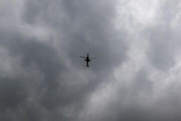 Silhouette of an AH-64 Apache helicopter flying against a cloudy sky