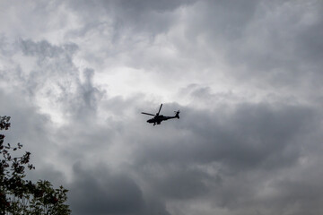 Silhouette of an AH-64 Apache helicopter flying against a cloudy sky