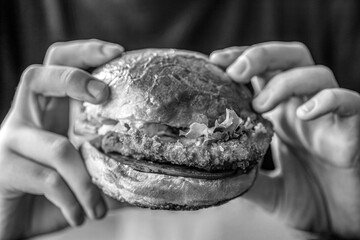 Man hands holding burger with meat, cheese and vegetables. Man holds burger with hands. Black and white