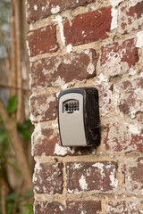 Detailed view of a grey lockbox with numeric code fixed on rustic red bricks.