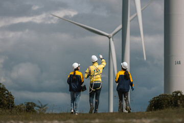 Group of wind energy engineers in safety inspecting wind turbines on green field. Concept of teamwork in renewable energy, sustainable development, green job and clean power industry collaboration.