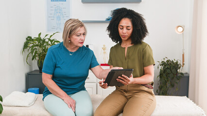 Physiotherapist Guides Senior Woman Through Tablet-Assisted Therapy Session In A Modern Clinic