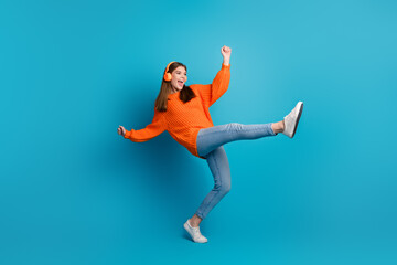 Obraz premium Charming young girl in bright orange sweater enjoying music with headphones on a vibrant blue background