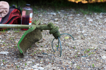 Green grass trimmer tool lie on gravel ground with blurred background