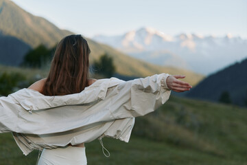 A lone person stands in a expansive meadow with arms outstretched, facing distant mountains under a...