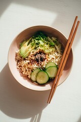 Cold ramen salad bowl with cucumbers, lettuce, avocado slices, and sesame dressing in pastel bowl