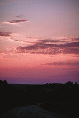 A picturesque sunset scene featuring a vibrant pink and purple sky. Silhouetted trees and land are visible in the foreground, creating a tranquil and serene atmosphere.