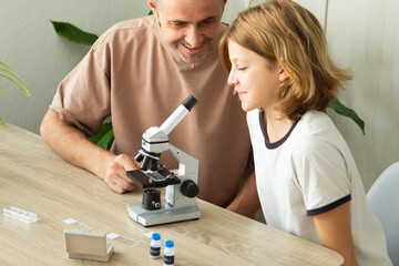 Father and daughter explore biology at home using a microscope to study plant specimens
