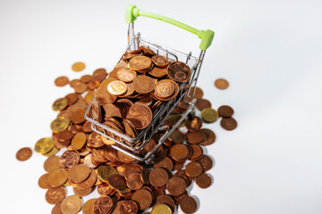 Mini shopping cart filled with euro cent coins, surrounded by scattered coins, symbolizing savings,...