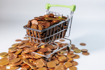 Mini shopping cart filled with euro cent coins, surrounded by scattered coins, symbolizing savings,...