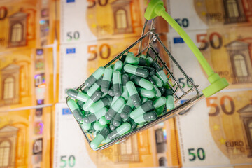 A miniature shopping cart filled with green capsules placed on 50 euro banknotes, symbolizing healthcare costs, pharmaceutical business, and drug market value.