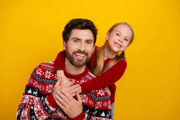 Father and daughter in festive sweaters embrace with joy on a vibrant yellow background, radiating...