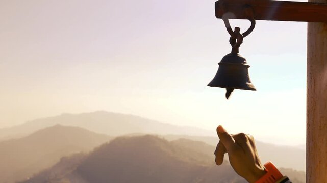 A serene slow-motion footage of a hand ringing a temple bell in a small village of Uttarakhand, with majestic mountains in the background. The soothing chime symbolizes spirituality and devotion.