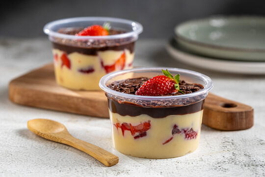 Dessert in a delivery pot made with vanilla cream, strawberries and chocolate topping.