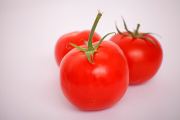Three ripe red tomatoes with green stems against a soft white background.