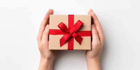 Top view of hands holding a gift box with a red ribbon on a white background