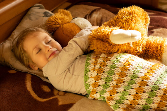 smiling little girl with closed eyes hugging her teddy bear toy slepping on the bed
