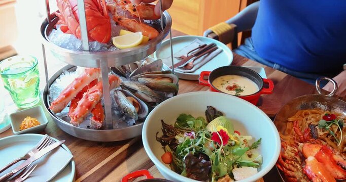 Seafood platter with lobster, king crab, mussels on ice, mixed salad, and creamy chowder on restaurant table, gourmet dining experience, coastal cuisine, vibrant colors.