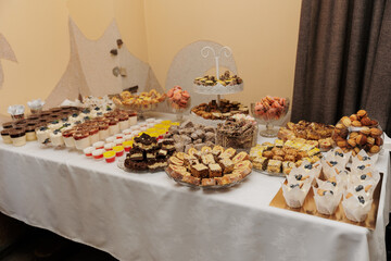 Wedding dessert table with a variety of sweets: cakes, muffins, jelly, rolls, cookies, and macarons. Bright and appetizing arrangement creating a festive atmosphere.