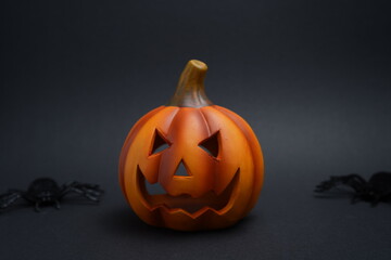 Halloween jack-o-lantern with carved spooky face surrounded by black spiders on dark background. Creepy seasonal decoration symbolizing festive horror theme.