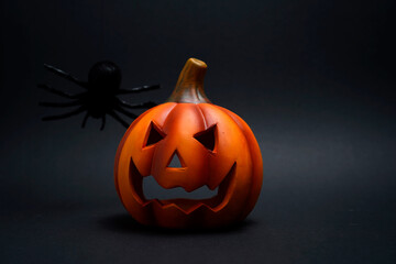 Halloween pumpkin lantern with carved face and black spider on top against dark background. Creepy festive symbol creating spooky holiday atmosphere.