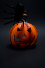 Halloween pumpkin lantern with carved face and black spider on top against dark background. Creepy festive symbol creating spooky holiday atmosphere.