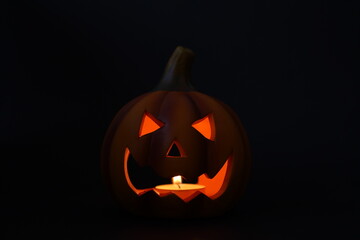 Glowing carved pumpkin lantern with candle inside on dark background. Classic Halloween decoration creating spooky and festive atmosphere with eerie expression.