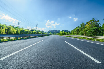 Empty asphalt highway road and green hills with a clear blue sky. Transportation and travel concept.