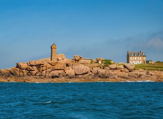 Picturesque view of the famous Ploumanac'h lighthouse (Mean Ruz) on the Pink Granite Coast in Brittany, France. The rugged shoreline with unique rose-colored granite rocks, a traditional French house