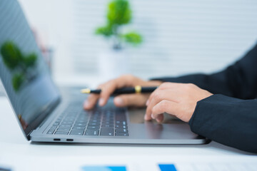 Asian businesswoman's hands typing on laptop keyboard and sitting in office