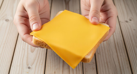Hands holding a slice of yellow cheese on a piece of bread, showcasing a simple meal preparation process with wooden table background and natural lighting