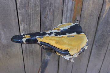 torn old bicycle saddle, The upholstery of the bicycle saddle is torn. The soft yellow foam is visible.