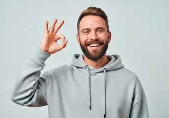 Naklejka na ściany i meble Bearded man in a grey hoodie giving an ok sign with a big smile, looking at the camera of mockup