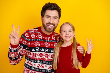 Father and daughter wearing Christmas sweaters joyfully posing together against vibrant yellow...