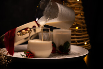 Pouring rompope into glass with christmas decorations and lights